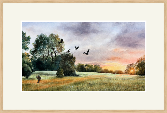 Framed artwork of a landscape with trees, field, and birds flying over at sunset.